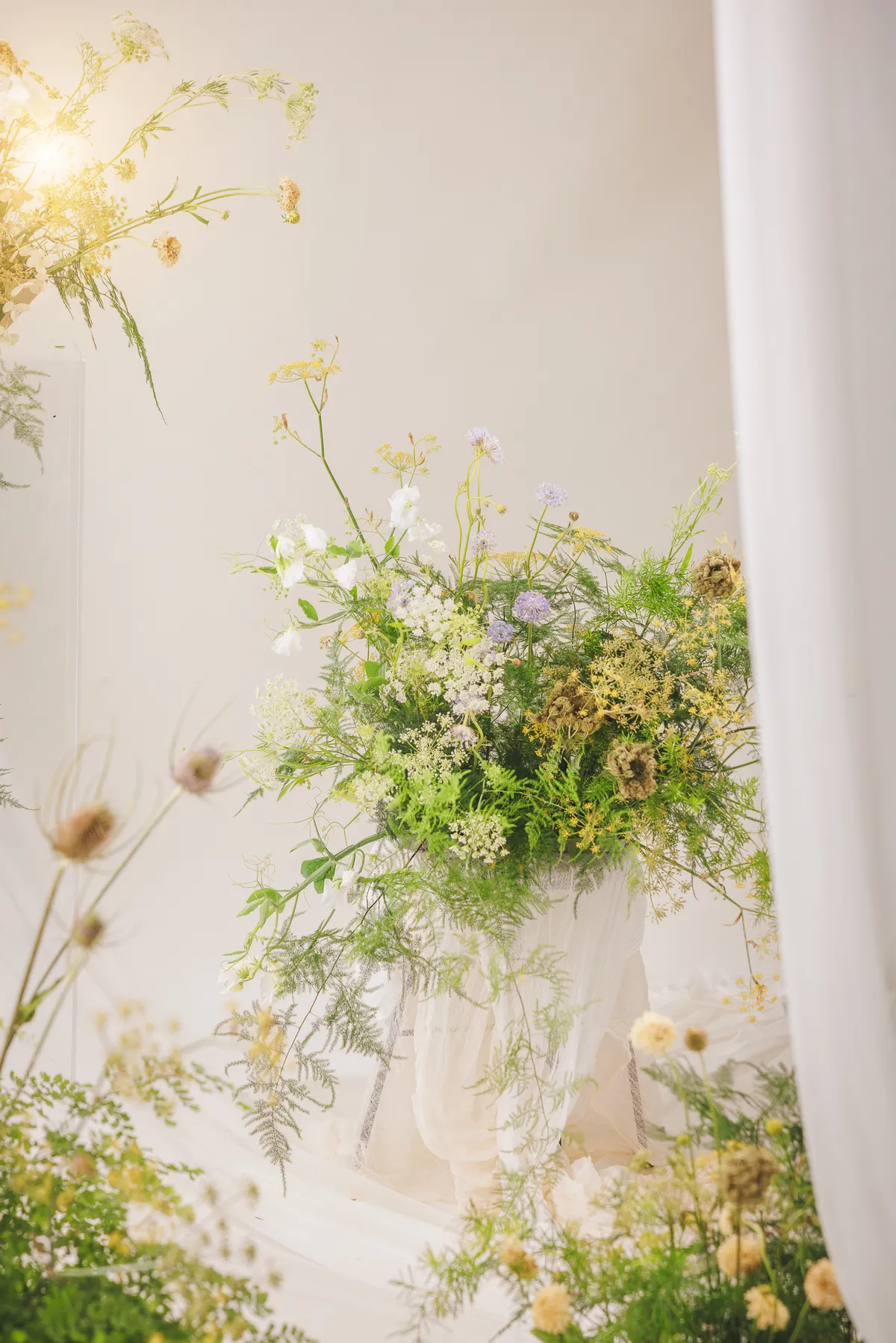 Loose wildflower arrangement of Queen Anne's lace, scabiosa and ferns in a draped vessel — Let Them Eat Flowers